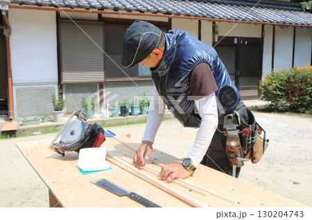 大工さんが作業台の上で細長い木材に鉛筆で印をつけている 130204743