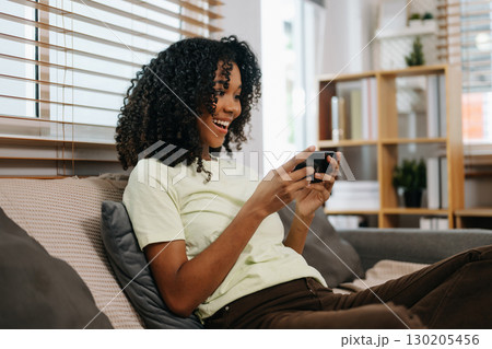 frican woman using the smartphone and tablet on the sofa at home 130205456