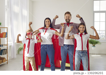 Happy family in superhero costumes standing with hands in fist and looking at camera at home. Happy family in superhero costumes standing with hands in fist and looking at camera at home. 130206201