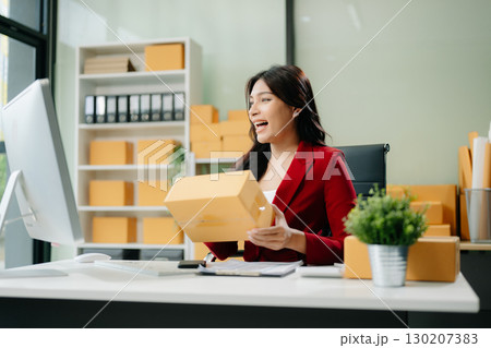 Asian woman prepares parcels and checks online orders on tablet and laptop for delivery online shopping 130207383