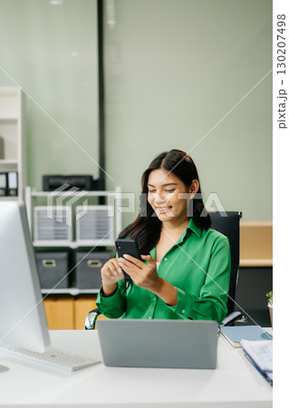 Young attractive Asian female office worker business suits smiling in office Young attractive Asian female office worker business suits smiling in office 130207498