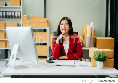 Asian woman prepares parcels and checks online orders on tablet and laptop for delivery online shopping 130207620