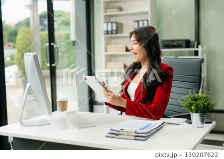 Asian woman using laptop and tablet while sitting at her working place Asian woman using laptop and tablet while sitting at her working place 130207622