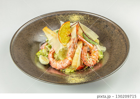 Caesar salad with grilled shrimp, parmesan cheese, croutons, and orange slice on a dark plate 130209715