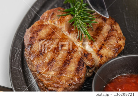 Close up of grilled beef steak with rosemary and sauce on a black plate Close up of grilled beef steak with rosemary and sauce on a black plate 130209721