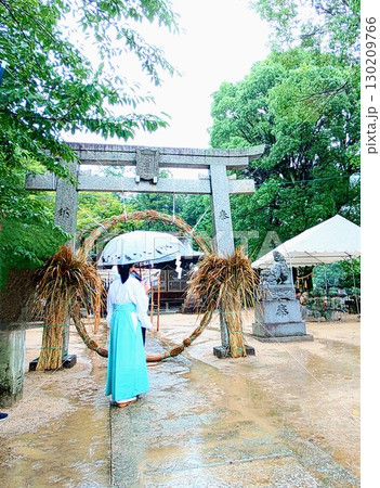 雨の日の茅の輪くぐり、樹々の緑と鳥居と大きな茅の輪、水色の袴をはいて傘をさす巫女さんの姿、近所の神社 130209766