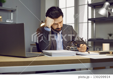 Male auditor or accountant gets tired while working with documents in the office 130209914