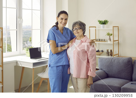 Young smiling nurse caregiver supporting and hugging senior woman patient at home. 130209958