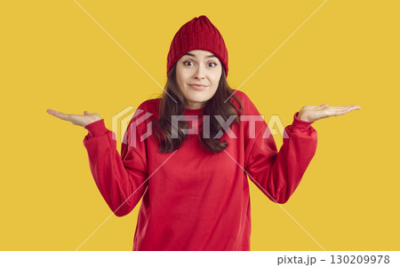 Clueless woman in red sweatshirt and hat shrugs shoulders isolated on yellow background Clueless woman in red sweatshirt and hat shrugs shoulders isolated on yellow background 130209978