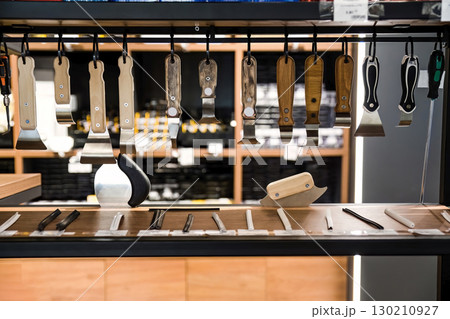 Wooden and plastic handled spatula tools hanging on display in a hardware store, used for stretch ceiling installation and PVC film fitting. 130210927