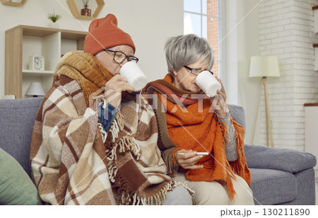 Sick senior couple covered in blankets sitting on sofa at home with seasonal flu or cold. Sick senior couple covered in blankets sitting on sofa at home with seasonal flu or cold. 130211890
