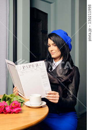 Woman reading menu in a cozy cafe, enjoying coffee and flowers during daytime 130211998