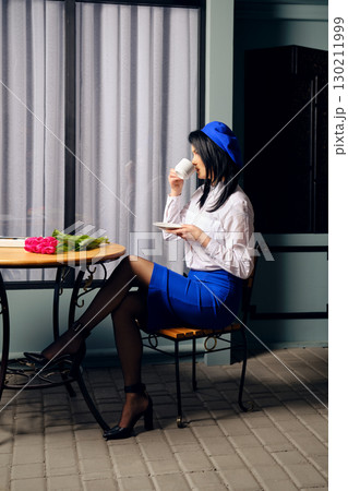 Stylish woman enjoying coffee at a cafe table with flowers and greenery during the day 130211999