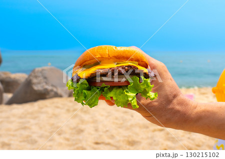 Man holding burger in a hand against beach background 130215102