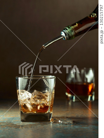 Whiskey is poured from a bottle into a frozen glass with natural ice. Whiskey is poured from a bottle into a frozen glass with natural ice. 130215797