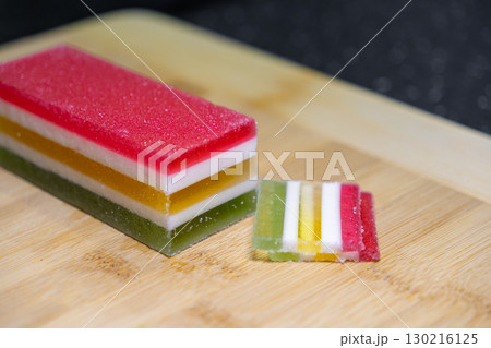 Delicious colorful layered jelly cake showcasing vibrant red, white, yellow, and green hues, perfect for festive dessert or sweet snack 130216125