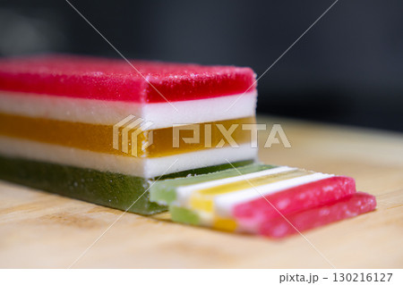Vibrant layered jelly candy block with cut slices, showcasing red, white, yellow, and green colors, representing delicious confectionery treat or festive snack Vibrant layered jelly candy block with cut slices, showcasing red, white, yellow, and green colors, representing delicious confectionery treat or festive snack 130216127