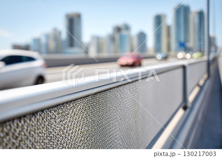 Close-up of textured sound-absorbing barrier with city skyline and blurred traffic in natural daylight Close-up of textured sound-absorbing barrier with city skyline and blurred traffic in natural daylight 130217003