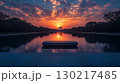 Reflecting pool mirroring ancient columns and dramatic sunset sky with glowing orange clouds. Serene water surface creating symmetrical architectural reflection 130217485