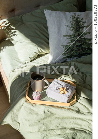Wooden tray with coffee, candle and gift present on bed duvet. 130219573