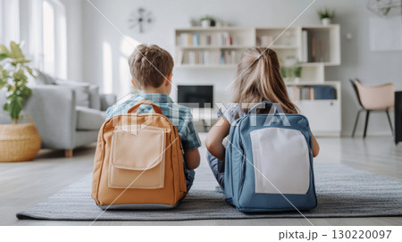 Children with school backpacks sitting on floor in bright room 130220097