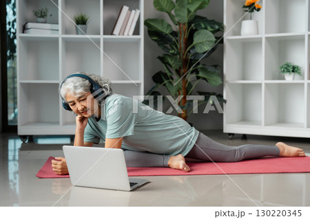 Senior woman practicing wellness and stretching at home with online fitness class on laptop Senior woman practicing wellness and stretching at home with online fitness class on laptop 130220345