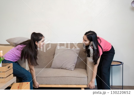 LGBT couple joyfully moving a couch together into their new home, teamwork on display 130220652