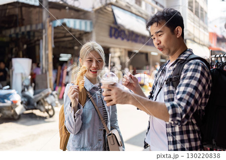 Couple enjoying snacks and drinks at a lively street market. Couple enjoying snacks and drinks at a lively street market. 130220838