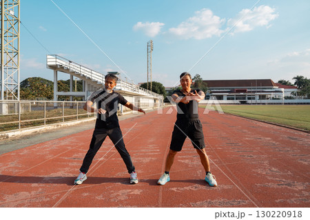 Two senior men performing wellness exercises and stretching at the athletic track Two senior men performing wellness exercises and stretching at the athletic track 130220918