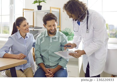 Friendly gynecologist advises couple on pregnancy and shows them clipboard with test results. Friendly gynecologist advises couple on pregnancy and shows them clipboard with test results. 130220933