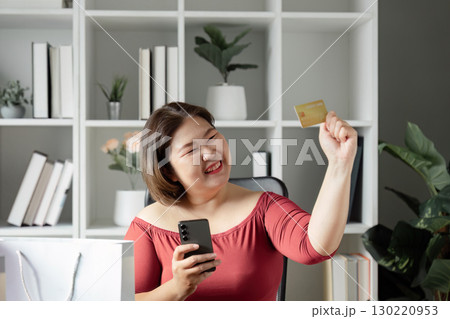 Joyful woman celebrating online shopping success, holding a credit card and smartphone with excitement 130220953