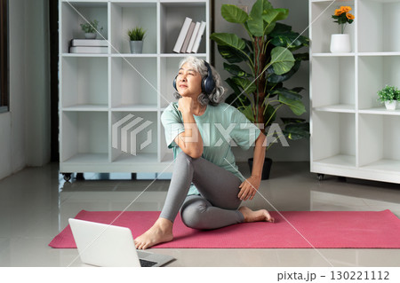 Senior woman practicing wellness with headphones and yoga mat in a modern space Senior woman practicing wellness with headphones and yoga mat in a modern space 130221112