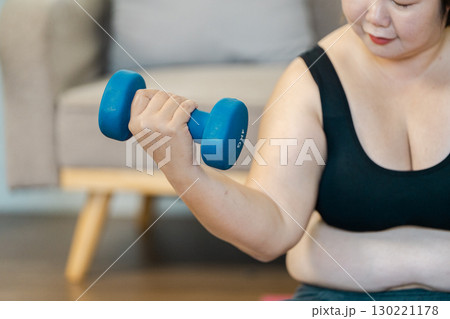 Overweight woman lifting weights at home, focusing on wellness and strength training Overweight woman lifting weights at home, focusing on wellness and strength training 130221178