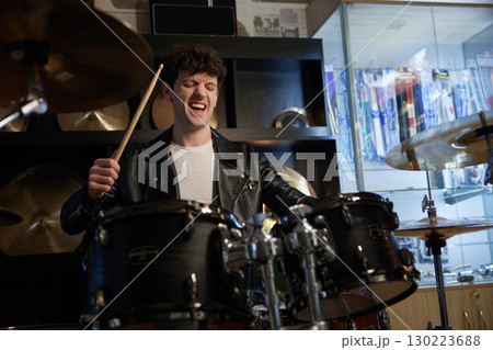 A man wearing a stylish leather jacket is energetically playing the drums 130223688