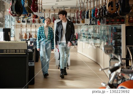 A man and a woman walk through a guitar store, exploring instruments A man and a woman walk through a guitar store, exploring instruments 130223692