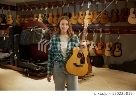 A woman is holding a guitar in front of a wall of guitars A woman is holding a guitar in front of a wall of guitars 130223819