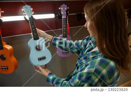 A young girl dressed in a plaid shirt is holding a blue ukulele guitar in her hands 130223820