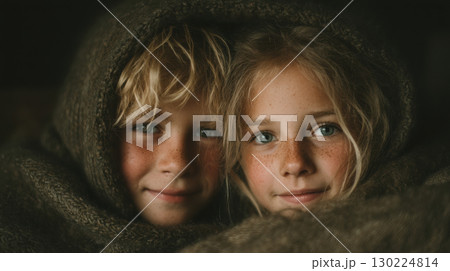 Two children with freckles wrapped in cozy wool blanket, sharing warm and intimate moment. Their expressions are gentle and serene 130224814
