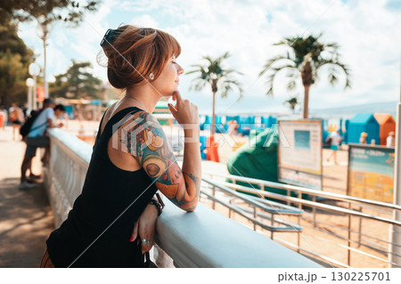 Portrait of a young smiling woman with a tattoo on her arm, looking at the sea. There is a beach in the background. The concept of summer vacation Portrait of a young smiling woman with a tattoo on her arm, looking at the sea. There is a beach in the background. The concept of summer vacation 130225701