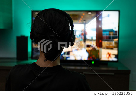 Young guy gamer in headphones plays on the console close-up rear view. Young guy gamer in headphones plays on the console close-up rear view. 130226350