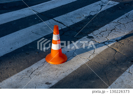 Traffic cone placed on uneven crosswalk highlighting urban infrastructure flaws under warm afternoon light 130226373