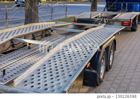 A trailer sits beside the road, displaying metal construction with a perforated surface and a sturdy build during a sunny day 130226398
