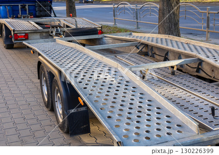 A heavy-duty car hauler sits parked on a city street, displaying its metal ramps and wheels under the afternoon sunlight A heavy-duty car hauler sits parked on a city street, displaying its metal ramps and wheels under the afternoon sunlight 130226399
