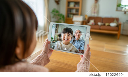 リビングで孫の女の子と祖父がオンラインビデオ通話を楽しむシーン|自宅の暖かな雰囲気 リビングで孫の女の子と祖父がオンラインビデオ通話を楽しむシーン|自宅の暖かな雰囲気 130226404