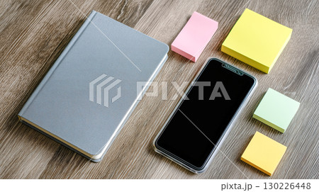 木目デスク上のノートブックとスマホ、カラフル付箋が並ぶオフィス風モダンな作業スペース 130226448