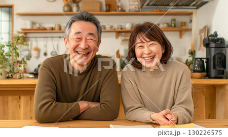 和やかな熟年夫婦が自宅キッチンで笑顔｜木製カウンターと観葉植物が映える温かい家庭風景 130226575