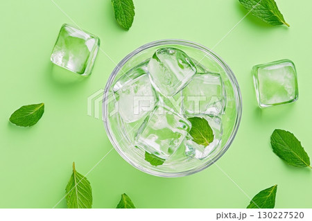 Refreshing drink with ice cubes and mint leaves on a vibrant green background perfect for hot days 130227520