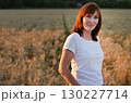 Woman stands in a golden field of wheat during sunset, showcasing natural beauty and serenity in a rural setting 130227714