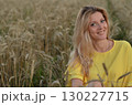 Woman sitting in a golden wheat field during sunset, capturing a serene moment of connection with nature under warm light 130227715