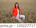 Woman sitting in a golden wheat field during sunset, capturing a serene moment of connection with nature under warm light 130227717